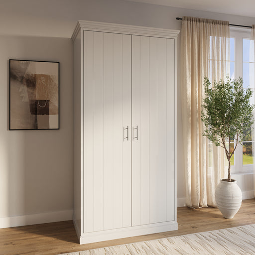 A white double wardrobe with two doors, situated in a room with a window, a painting, and a potted plant.