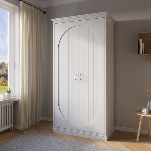 A white double arched wardrobe in a room with a window, curtains, and a small round table with a lamp next to the wardrobe.