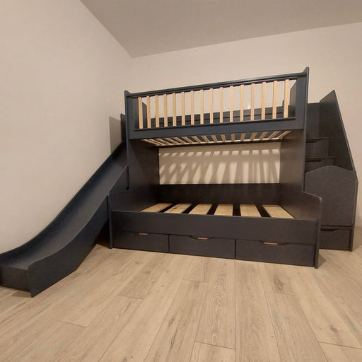 A deluxe bunk bed with slide in a room, featuring a dark gray or black finish, with stairs and storage drawers underneath.