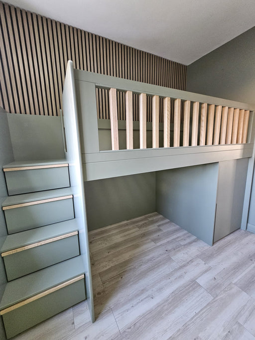 A mid-sleeper cabin bed with green walls, wooden sleepers, and gray stairs with gold handles. The bed is set against a gray background with wood paneling.