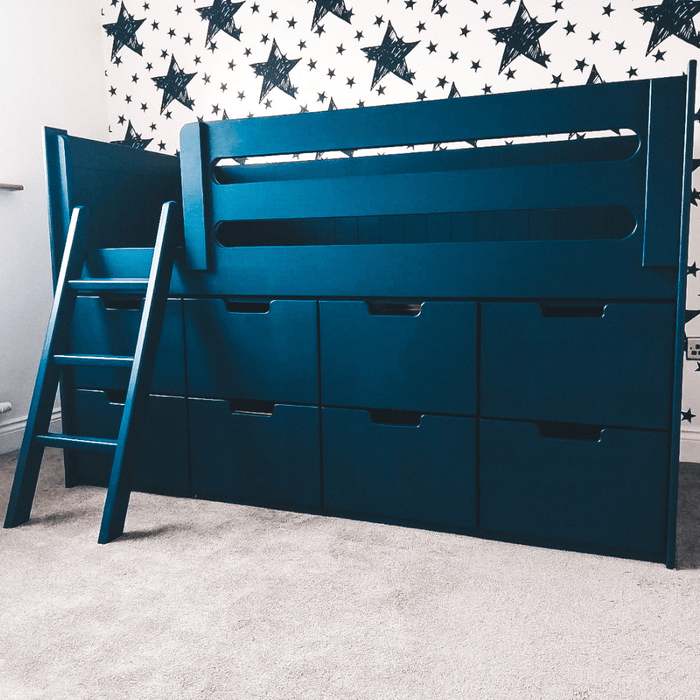 A blue toddler cabin bed with storage drawers and a ladder, placed in a room with star-patterned wallpaper.