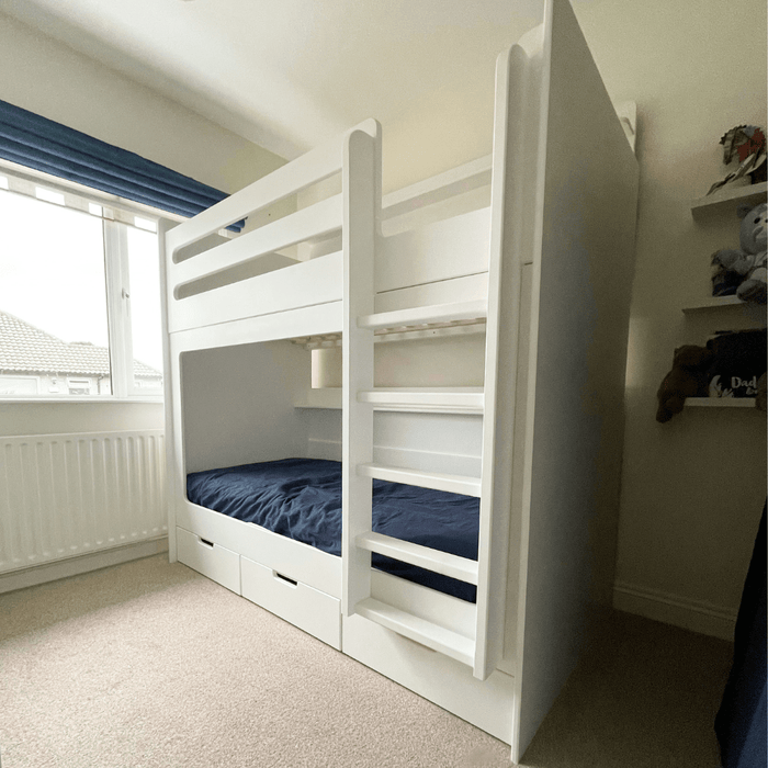 White wooden bunk bed with storage drawers and an integrated ladder in a child's bedroom.