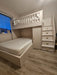 White loft bed with stairs in a room with wooden flooring and a window.