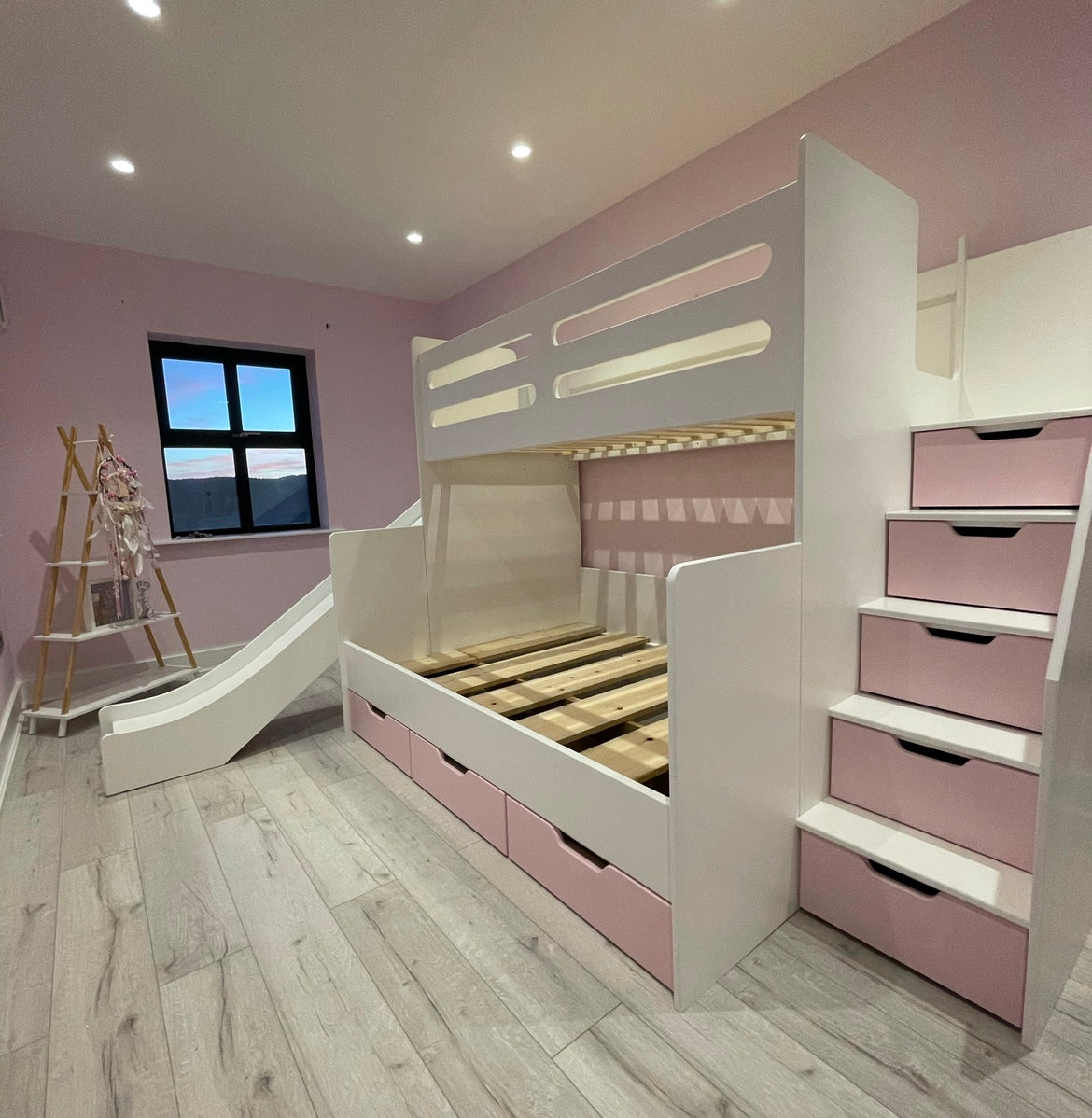 White and pink bunk bed with built-in storage drawers, a staircase, and a slide in a pink bedroom.